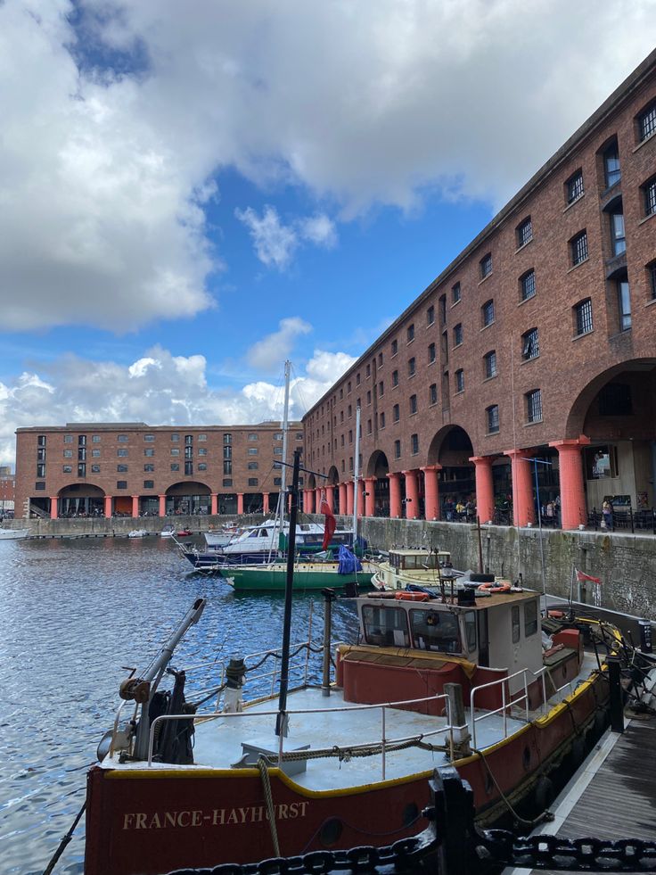 several boats are docked at the dock in front of some large brick buildings and water