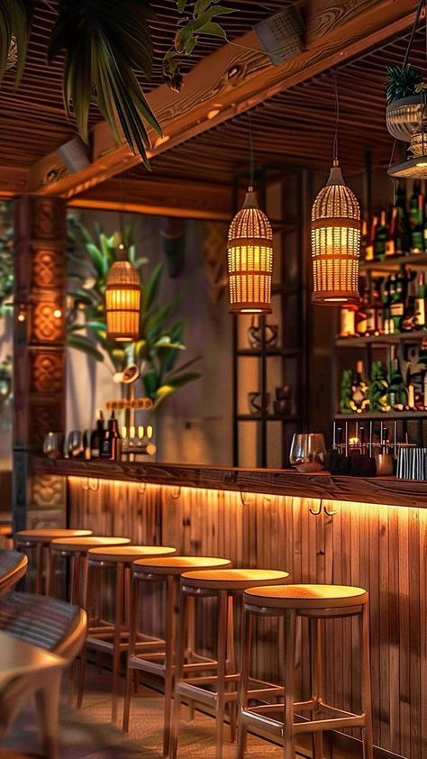 an empty bar with wooden stools and hanging lights above it, surrounded by tropical plants