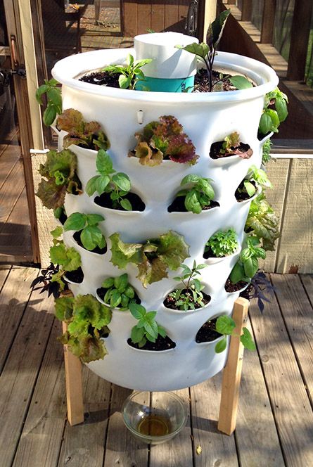 a tall white planter filled with plants on top of a wooden deck