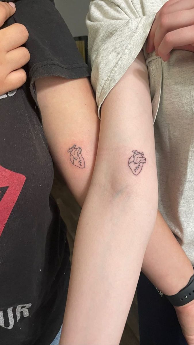 two people with tattoos on their arms and one has a small heart tattooed on the arm