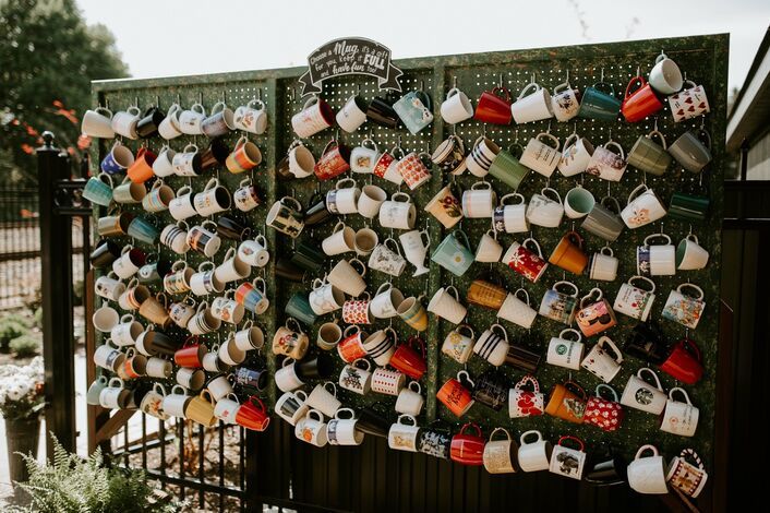 there are many mugs hanging on the side of this fence, which is decorated with tea cups