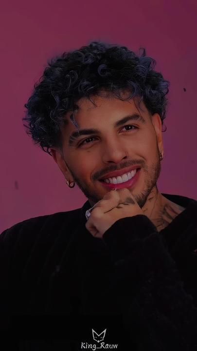 a man with curly hair and piercings smiling at the camera while wearing a black shirt