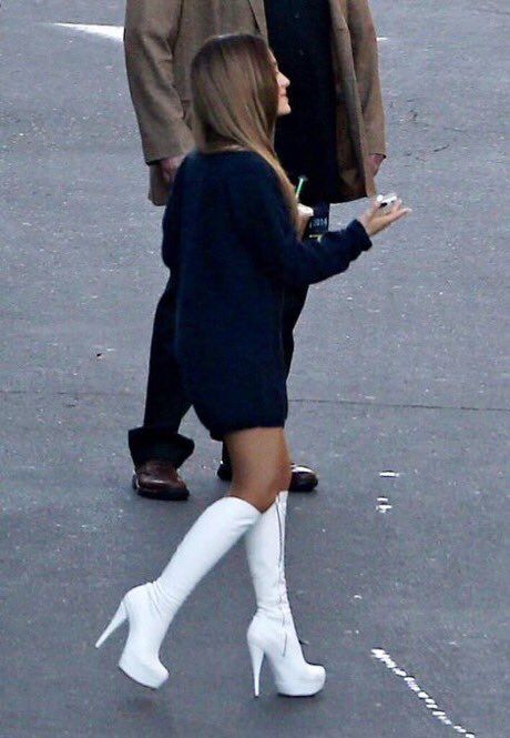 a woman in white boots walking down the street with a man wearing a brown coat