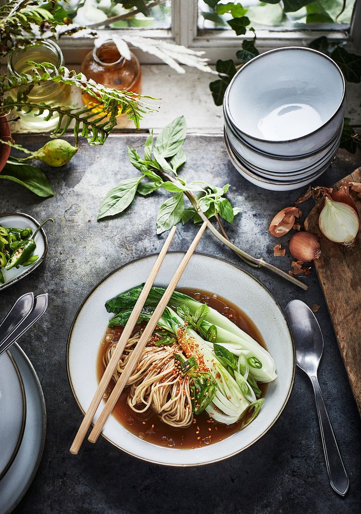 a bowl of soup with chopsticks and vegetables on a table next to plates