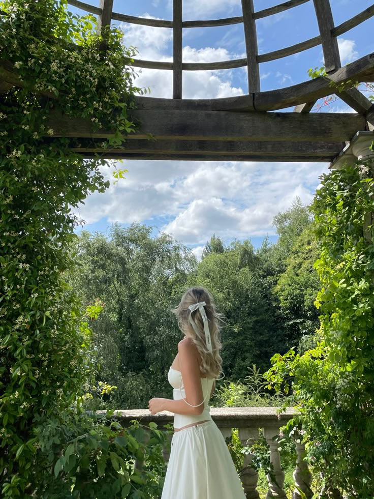 a woman in a white dress is standing on a wooden bridge and looking into the distance