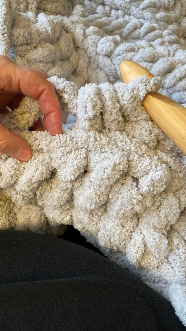 someone is crocheting the edges of a blanket with a wooden skewer