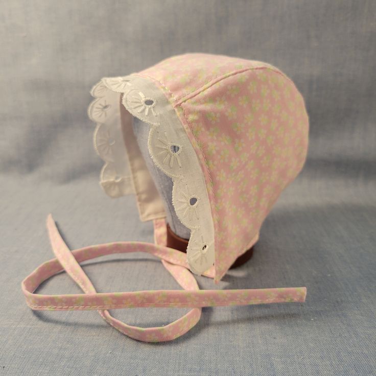 Made to Order. Crafted with love and care from 100% cotton and eyelet lace trim, this handmade cotton baby bonnet is a charming accessory for your little one. Made from soft, breathable cotton, it ensures comfort and style in one adorable package. The delicate craftsmanship of this bonnet adds a touch of artisanal flair to your baby's ensemble. Whether worn for a special occasion or as a daily accessory, this bonnet is both practical and delightful. Its timeless design and high-quality materials make it a thoughtful gift for new parents or a sweet addition to your baby's wardrobe. Add a touch of handmade beauty to your baby's look with this lovely cotton baby bonnet. Perfect for protecting your baby's delicate skin from the sun or wind, this bonnet is as functional as it is adorable. The a Handmade Cute Pink Bonnet, Cute Handmade Pink Bonnet, Handmade Cute Adjustable Bonnet, Handmade Adjustable Cute Bonnet, Cute Pink Cotton Bonnet, White Cotton Bonnet As A Gift, White Cotton Bonnet As Gift, Fitted Cotton Bonnet With Lace Trim, Handmade Cotton Hats As Gifts