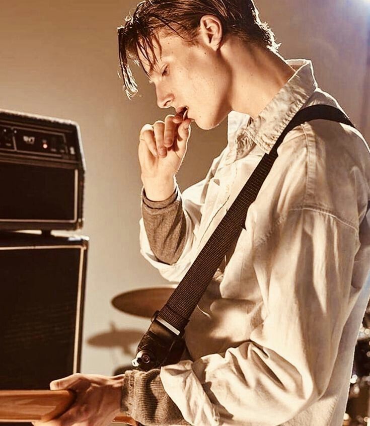 a young man holding a guitar in his right hand while standing next to an amp