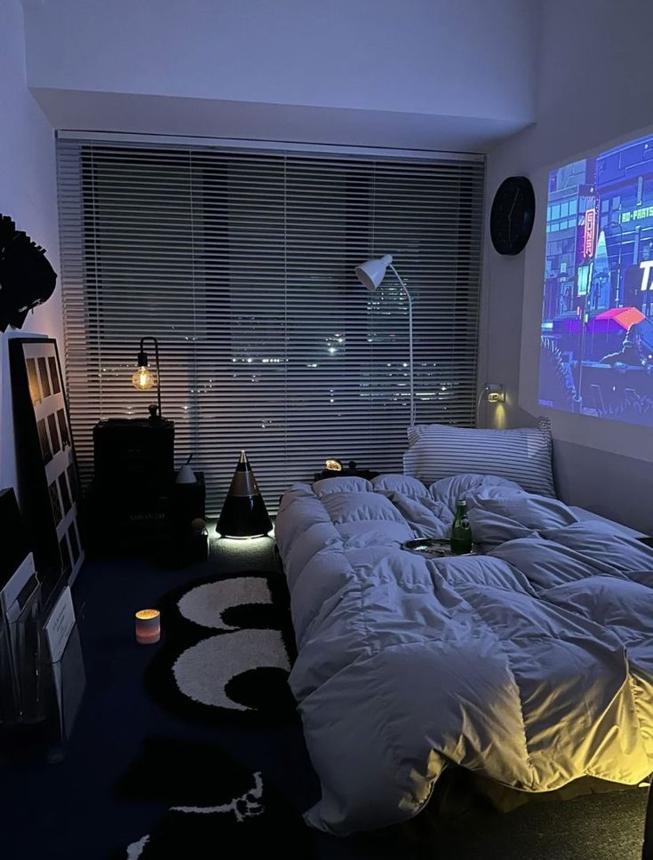 a bed with white sheets and pillows in front of a large screen on the wall