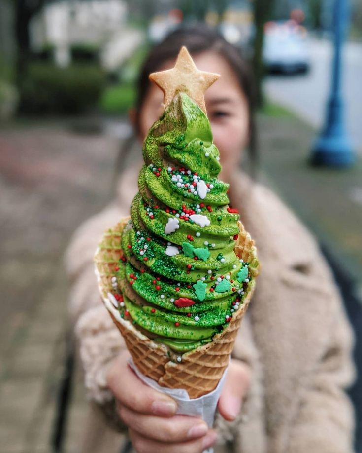 a woman holding an ice cream cone with green frosting and sprinkles