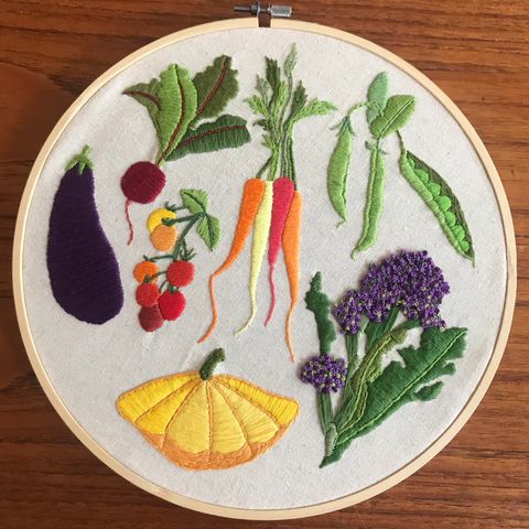 a close up of a embroidery on a wooden surface with fruit and veggies