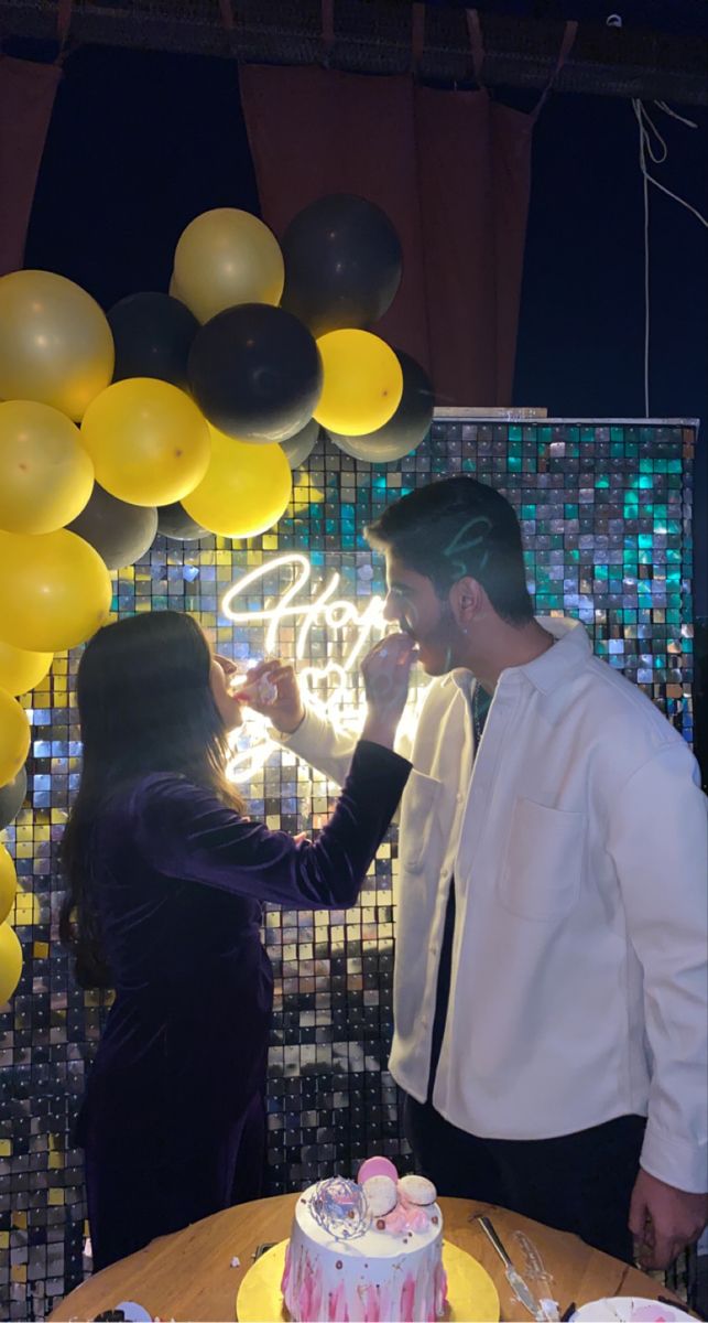 a man and woman standing next to each other in front of a cake with candles on it