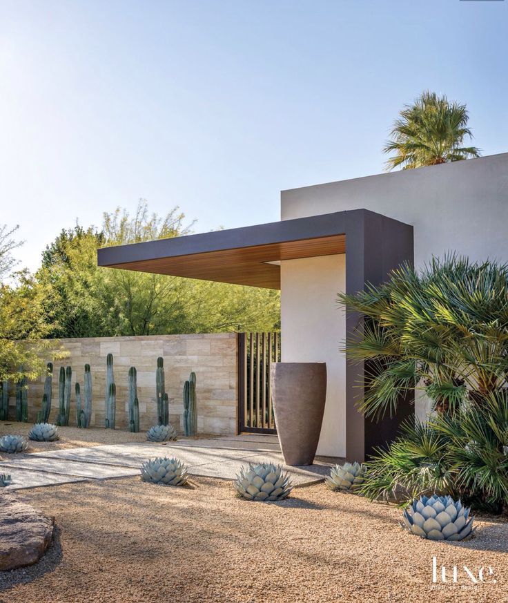 the front entrance to a modern home with cactus and trees in the yard, surrounded by rocks