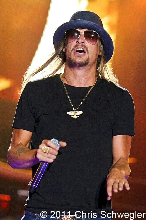 a man with long hair wearing sunglasses and a hat holding a microphone in his right hand