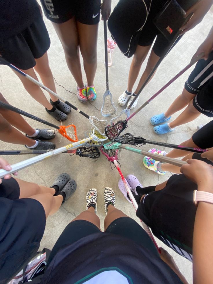 a group of people standing in a circle with their feet on the ground holding lacrosse sticks