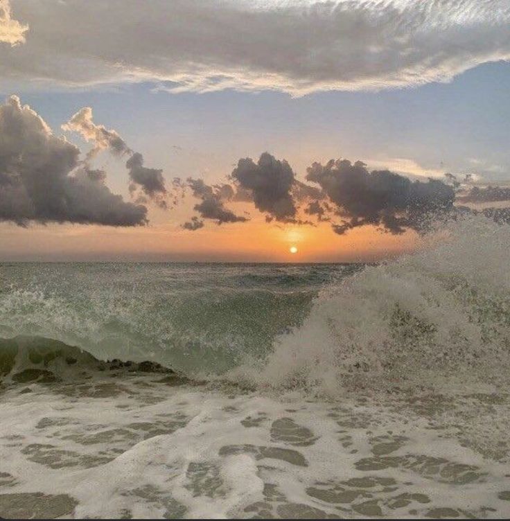 the sun is setting over the ocean with waves crashing in front of it and some clouds