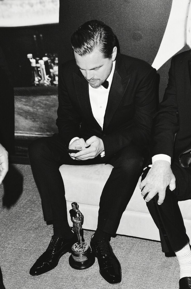 a man in a tuxedo sitting on a chair looking at his cell phone