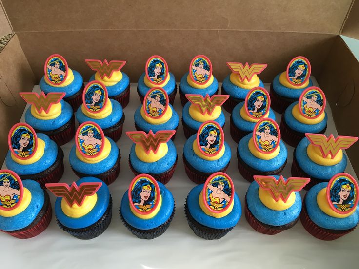 a box filled with cupcakes covered in blue frosting and wonder woman decorations