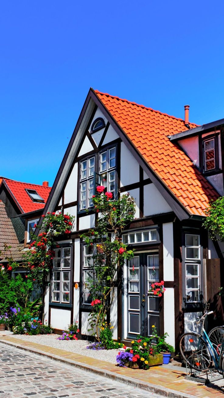 a bicycle parked in front of a white and brown house with red roof tiles on the street