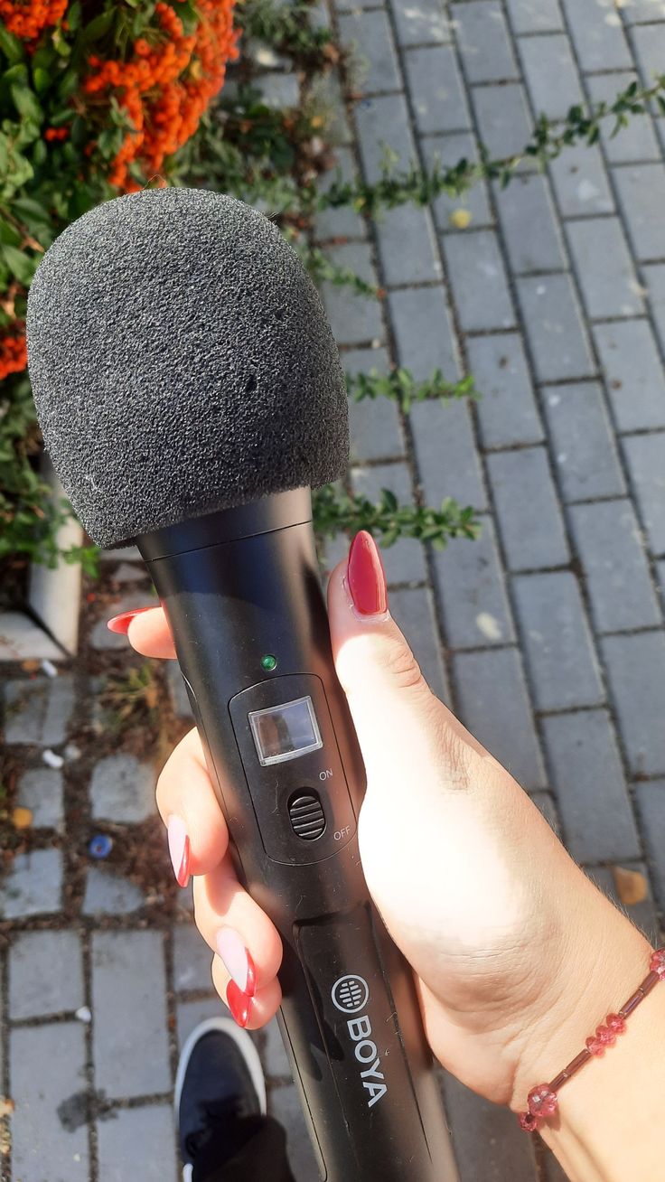 a woman is holding a microphone in her hand while standing on a brick walkway next to flowers