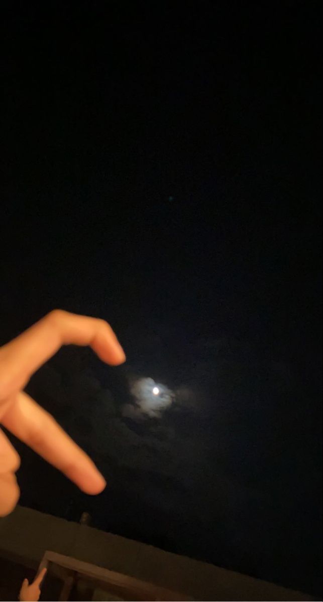 someone is pointing at the moon in the night sky with their hand out to the side