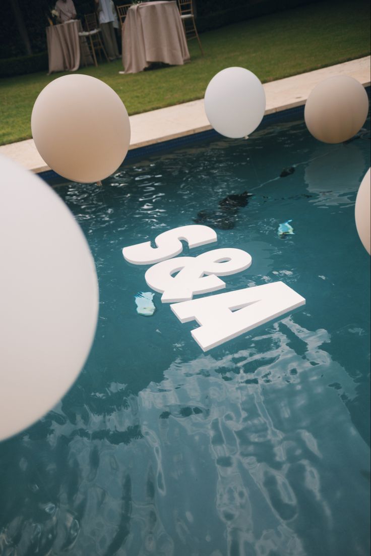 some white balloons floating in the water near a table with chairs and tables on it