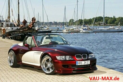 a red and white convertible car parked next to a body of water with boats in the background