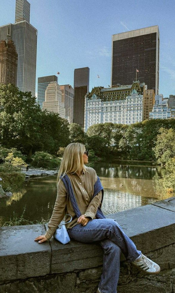 a woman sitting on the edge of a wall next to a river in a city