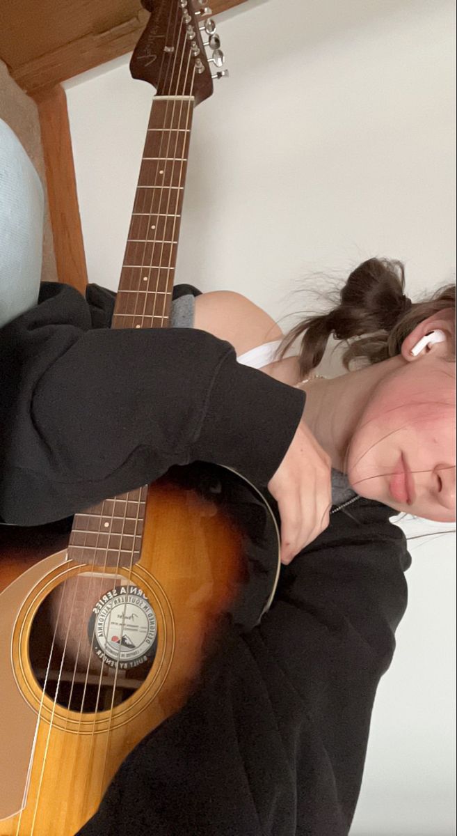 a person laying down with a guitar in front of their face and one hand on the neck