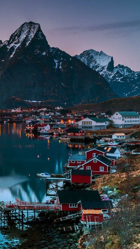 the mountains are covered in snow and there is a small town on the water with red houses