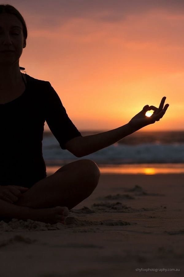 a woman is sitting on the beach with her hands in the air as the sun sets