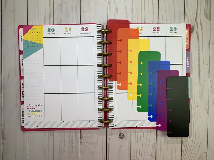 an open planner book on a wooden table with colorful paper and colored pencils next to it