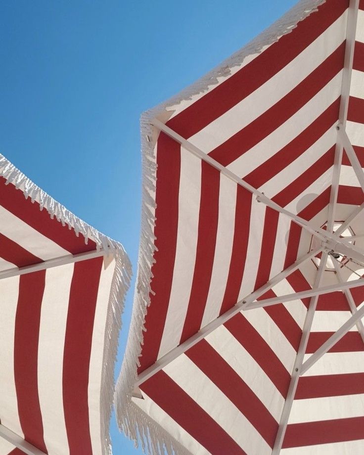 two red and white striped umbrellas with fringed edges against a blue sky background