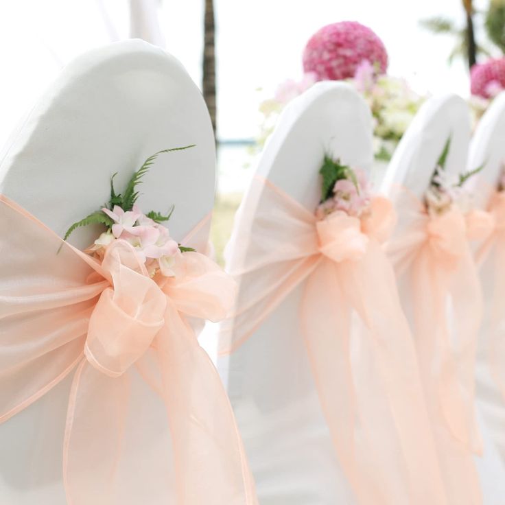 four white chairs with pink bows and flowers on the back are lined up in rows