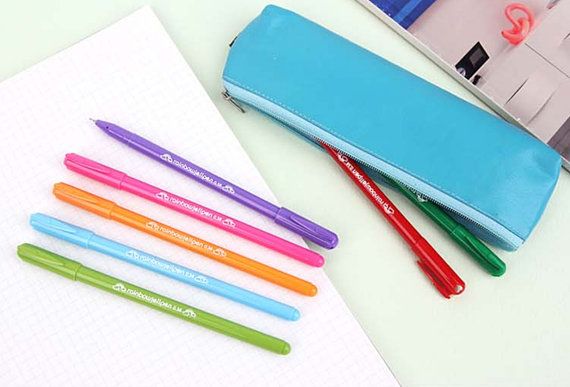 four different colored pens sitting on top of a notepad next to a pencil case