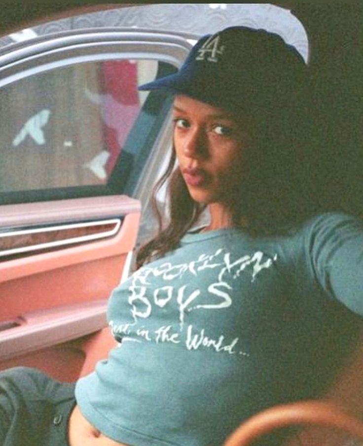 a woman sitting in the back seat of a car wearing a baseball cap and t - shirt