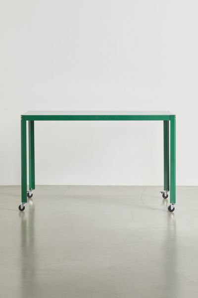 a green table sitting on top of a cement floor next to a white wall in an empty room