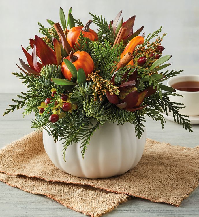 a white pumpkin vase filled with flowers on top of a table next to a cup of coffee