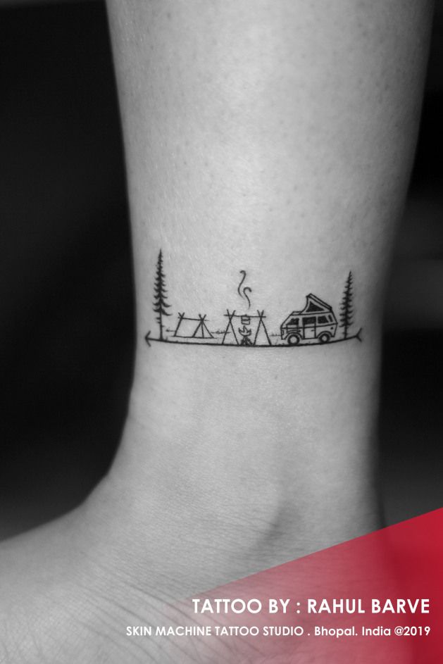 a small tattoo on the ankle of a person with a camper and trees in the background