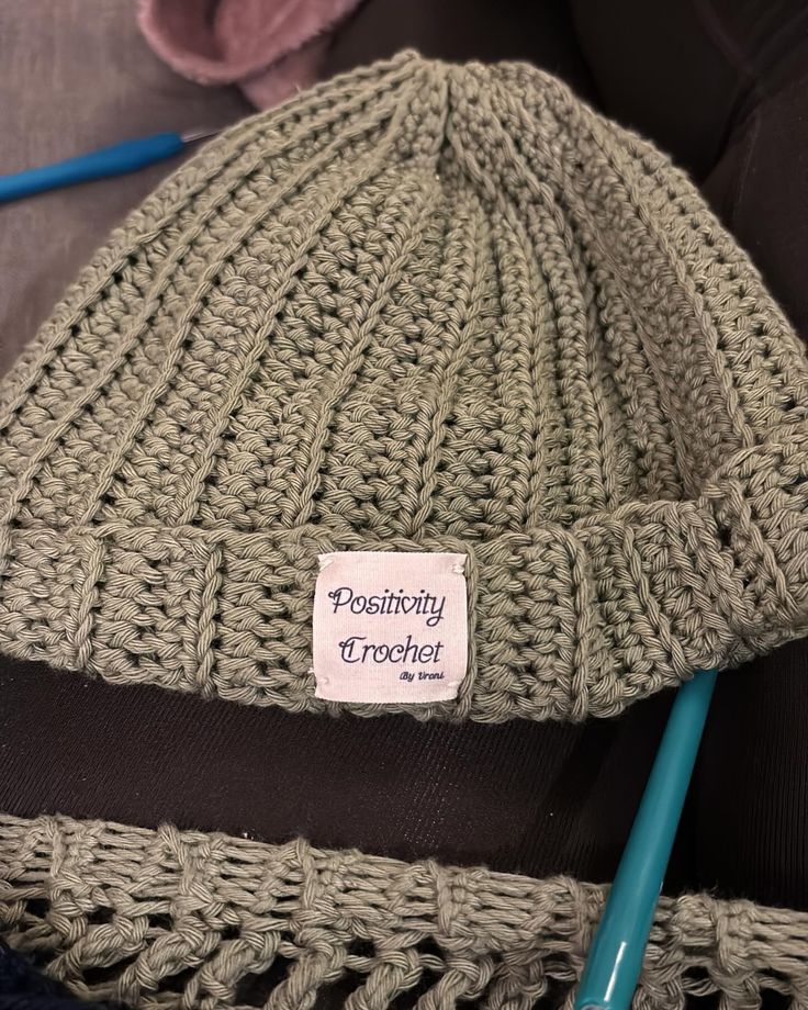 a knitted beanie with a sticker on it sitting next to some knitting needles