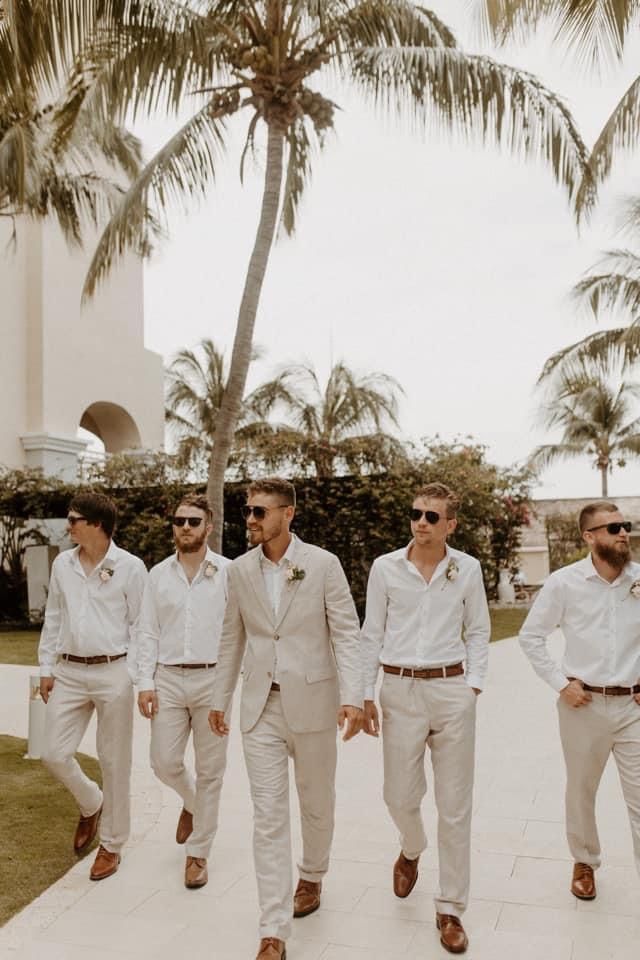 a group of men in white suits and sunglasses walking down a sidewalk next to palm trees