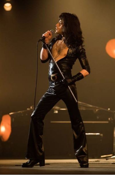 a man in black leather outfit holding a microphone and singing into a mic on stage