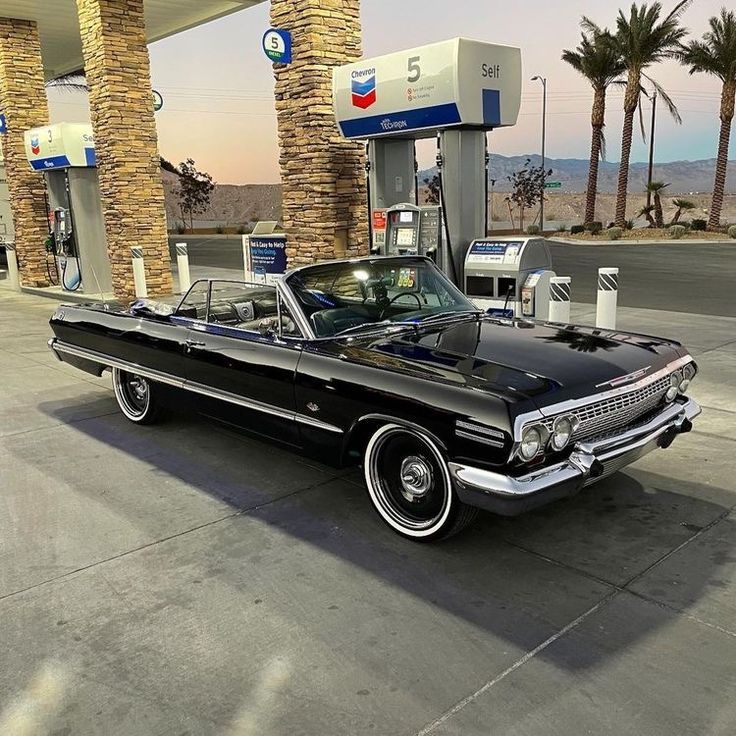 an old black car parked in front of a gas station