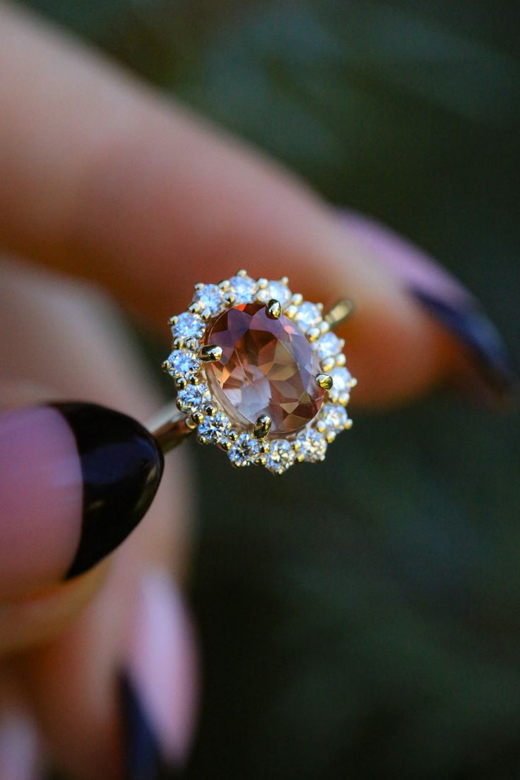 a close up of a person's hand holding a ring with an orange stone