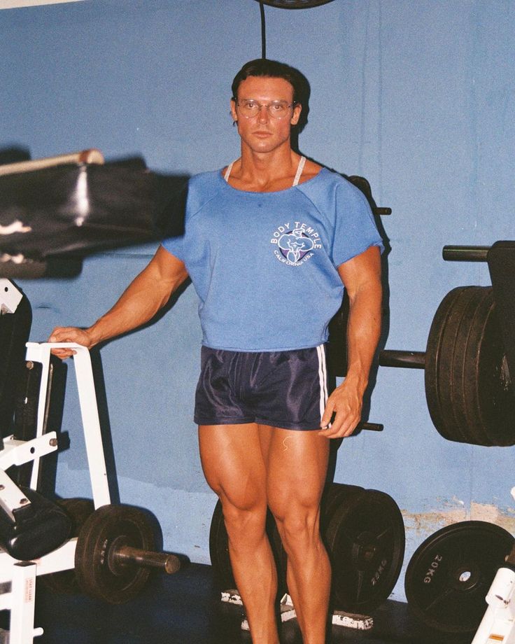 a man standing in front of a gym machine with his hands on the barbells