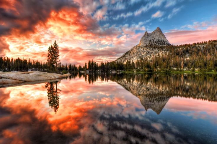 a mountain is reflected in the still water at sunset with red and blue clouds above it