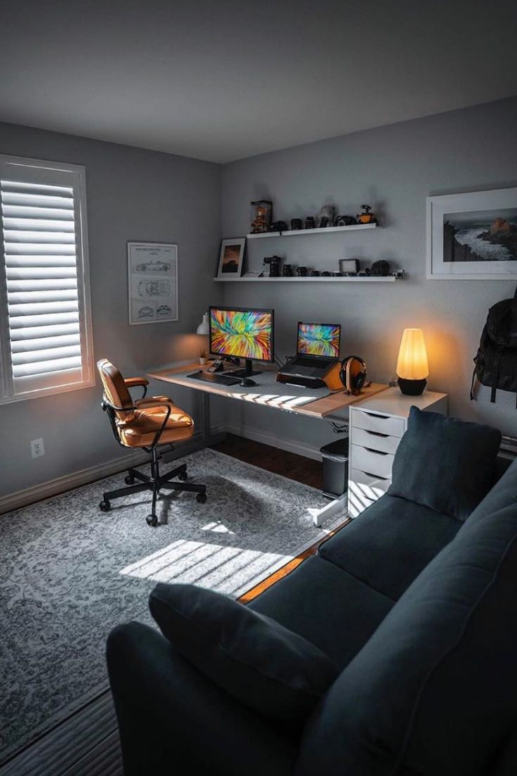 a living room with a couch, desk and two computer screens on the wall in front of it