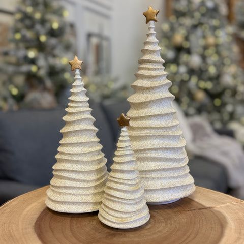 two white christmas trees sitting on top of a wooden table