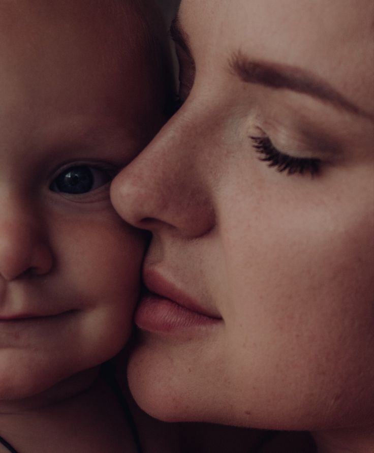 a close up of a woman kissing a baby's face with her eyes closed