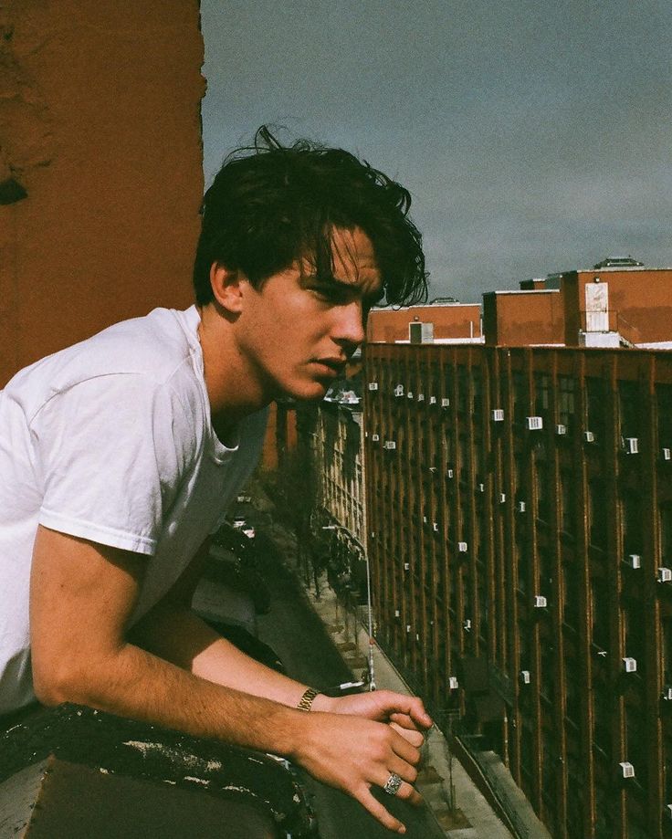 a man leaning on the side of a building with his hand on his hip while looking down